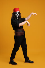 Fototapeta premium Man in scary pirate costume with skull makeup posing on orange background. Halloween celebration