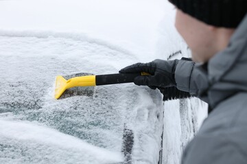 Man cleaning snow from car windshield outdoors, closeup