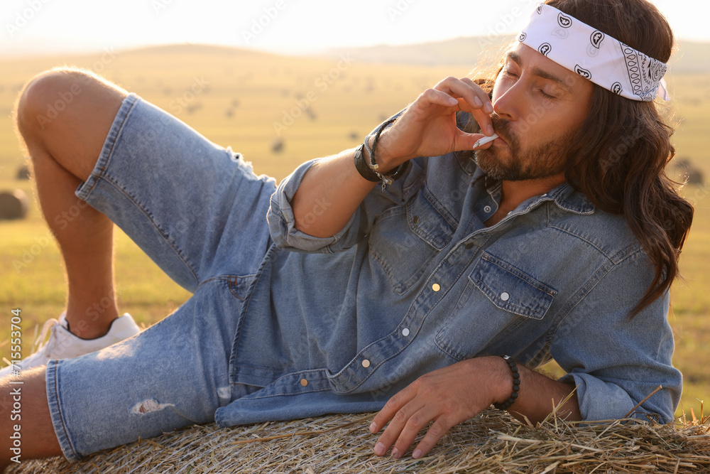 Wall mural Hippie man smoking joint on hay bale in field