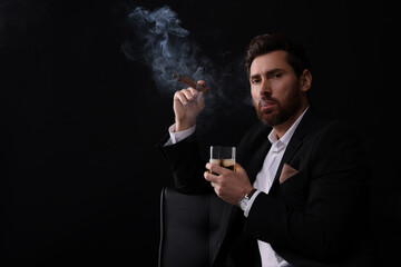 Handsome man in elegant suit with glass of whiskey smoking cigar on black background. Space for text