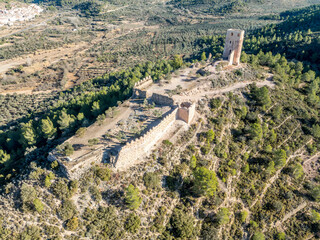 Fototapeta na wymiar Aerial view of Almonecir Castle, in the Sierra de Espadán above Vall de Almonacid, irrigated farmlands and an extensive olive groves with horseshoe shaped great tower partially restored