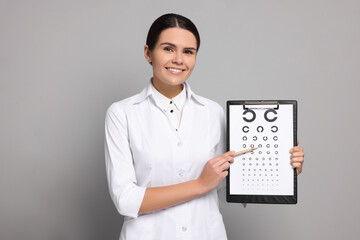 Ophthalmologist pointing at vision test chart on gray background