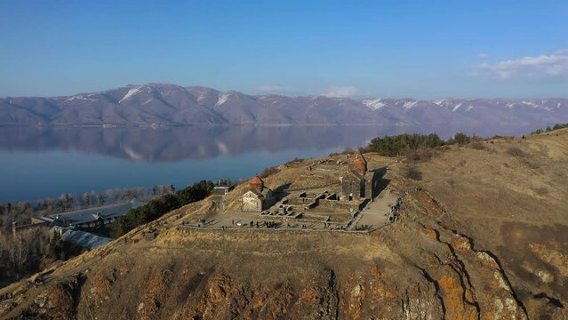 Medieval stone monastery on the shore of Lake Sevan. Aerial view church in Armenia. Drone fly above Ancient church, monastery․ Tourists near monastery. Famous touristic place.