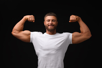 Young bodybuilder showing his muscular arms on black background