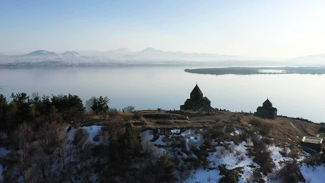 Medieval stone monastery on the shore of Lake Sevan. Aerial view church in Armenia. Drone fly above Ancient church, monastery․ Tourists near monastery. Famous touristic place.