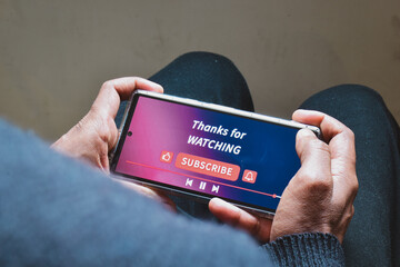 Man watching online streaming video footage on his smartphone. Channel subscriptions notification bell icon on Device screen. 