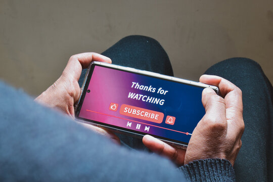 Man watching online streaming video footage on his smartphone. Channel subscriptions notification bell icon on Device screen. 