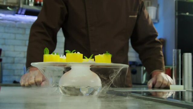 Chef in uniform presents dish with using of dry ice for smoky effect. Man uses special dish with dry ice on bottom with adiing hot water