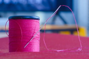 Sewing needle and pink thread roll on blurred background.