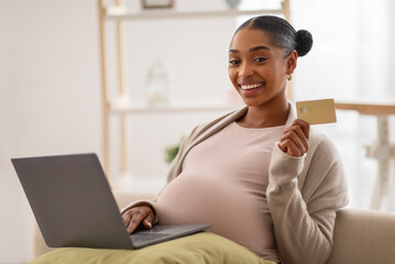 Positive black lady expecting baby, using laptop and credit card
