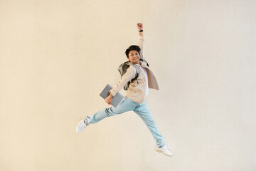 Excited young asian guy with laptop jumping in the air