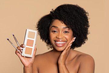 Joyful woman showcasing makeup palette and brushes