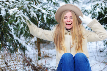 Beautiful young girl sitting on a sleigh, holding her hat and enjoying a beautiful snowy winter day 