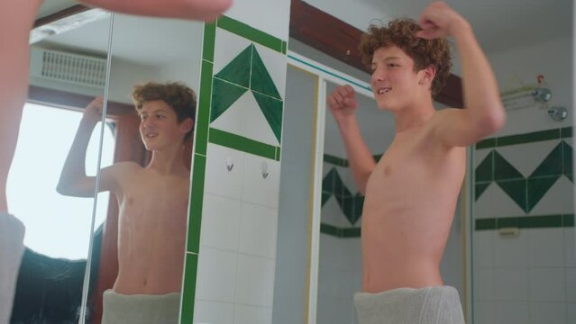A thinness teenager looks at his body in the mirror. The guy notices changes in his appearance, the teenager turns into a man. Awkward age. Puberty