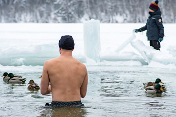 Boy or man with hat ice bathing in the freezing cold water of a frozen lake among ducks. Wim Hof Method, cold therapy, breathing techniques, yoga and meditation