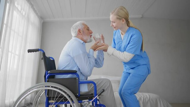 Nurse gives old wheelchair man pills. Physical therapist woman provides medical help support to paralyzed male gives water medications. Palliative care of neurodegenerative pathologies concept.