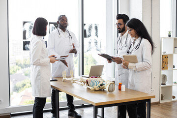 University, education, medicine, anatomy concept. Multiracial medical students with African American professor and human skeleton model in classroom, studying anatomy.