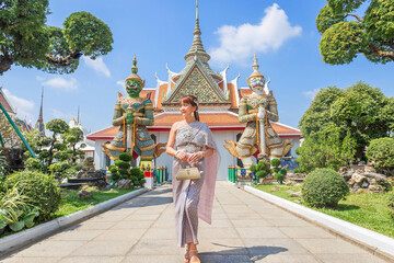 Young woman wearing traditional Thai dress stands holding an antique bag with giant front ornaments...
