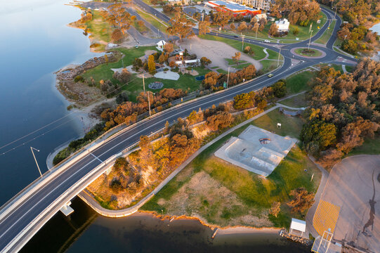 Aerial view of a curved road bridge over a river running into a roundabout in a parkland reserve