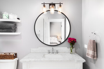A bathroom detail with a white cabinet, black circular mirror, and light fixture, and a view to the...