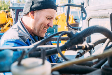 Mechanic repairs engine of tractor or heavy equipment. Farmer inspects and diagnoses agricultural machinery.