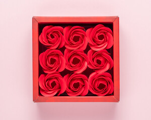 Red gift box with rose flowers on pink background. Minimal holiday concept.
