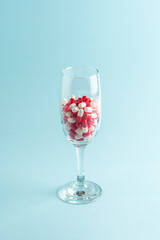 Creative view of wine glass with red pills on blue background. Minimal concept.