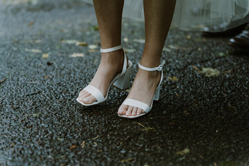 Slender womans feet in bridal or white shoes standing on the ground with her dress hitched up