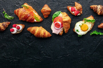Croissant sandwich assortment. Various stuffed croissants, overhead flat lay shot on a black slate background. Rolls filled with ham, salmon, egg, etc, with a place for text