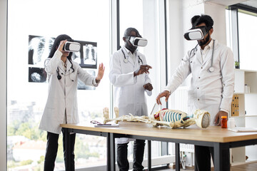 Human anatomy, VR, education, medicine concept. Young multiracial researchers using virtual reality goggles while working with human skeleton. Team of scientists in modern laboratory - obrazy, fototapety, plakaty