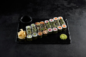 Assorted hosomaki sushi set with salmon, tuna, eel, and cucumber on black textured background