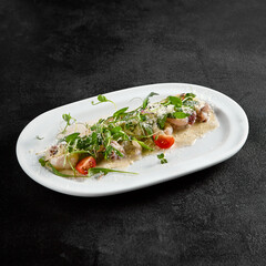 Creamy seafood assortment garnished with fresh greens and cherry tomatoes on a white oval plate