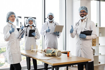 Multiethnic medical students in protective masks, gloves and hats on anatomy lesson in classroom...