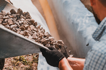 Drainage works for drainage of ground water. A man pours rubble crushed stone from a wheelbarrow...