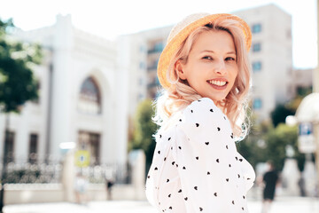 Closeup portrait. Young beautiful smiling blond woman in trendy summer white dress. Sexy carefree woman posing in street  at sunset. Positive model outdoors at sunny day. Cheerful and happy. In hat