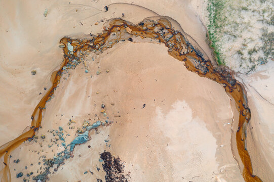 Aerial view of tannin stained creek winding its way over a sandy beach