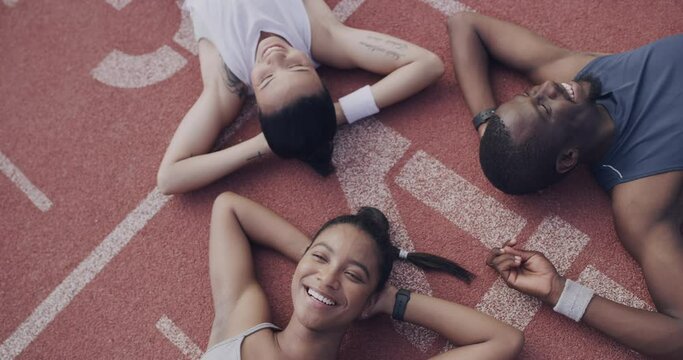 Happy people, sports and relax above on stadium track after workout, running or outdoor exercise together. Top view of young athletes smile and lying on floor on break for training, rest or recovery