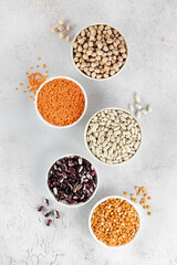 Various legumes. Red and white beans, lentils, peas and chickpeas in bowls on a gray table. Top view. Vegetarian food