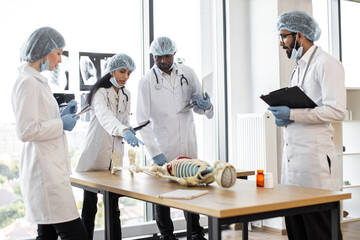 Human skeleton model on the table in classroom. Group of international medical students with Indian...