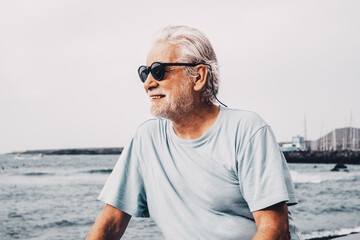 Portrait of carefree senior bearded man looking at horizon over water from sea beach at sunrise...
