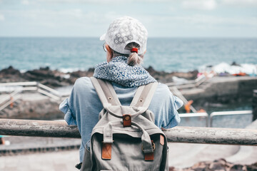 Rear view of senior traveler woman with cap looking at horizon over sea, elderly caucasian lady...