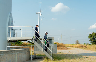 Two of technician workers walk down from stair of base of wind turbine or windmill after finish...