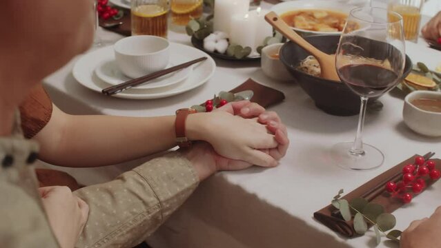 Cropped shot of unrecognizable couple holding their hands while dining with family at festive table at home