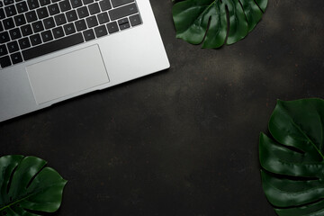 Workspace with laptop and palm leaves on black background. Flat lay, top view office table desk.