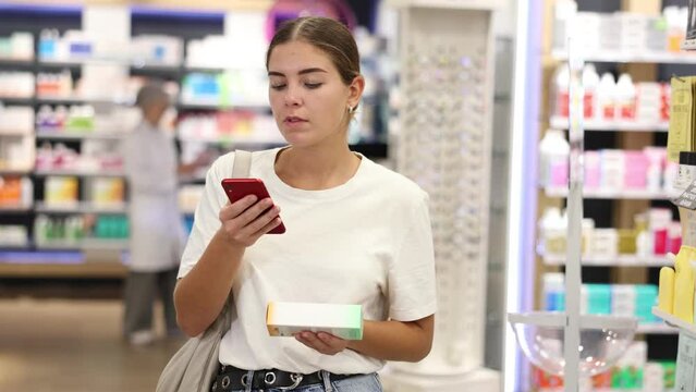 Interested young girl customer scanning QR of medical product held in hand in chemist's shop. High quality 4k footage