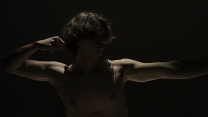Portrait of male model in studio on the black background under spotlight. Attractive man silhouette imitating archery bow at the camera.