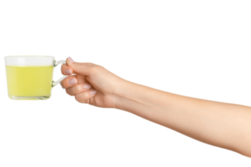 A woman's hand holds a cup of green herbal tea in a transparent glass cup. On a blank background