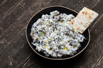 Armenian lavash chip in bowl of dip of eggplant with dill and yogurt.  Rustic wooden table. Copy...