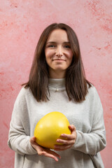 A young smiling woman holding whole pomelo fruit. 