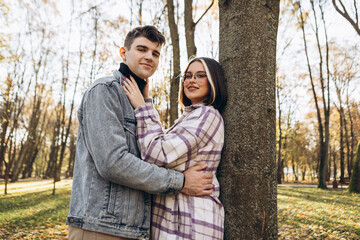 Heterosexual caucasian young loving couple walking outside in the city park in sunny weather, hugging smiling kissing laughing spending time together. Autumn, fall season, orange yellow red maple leav